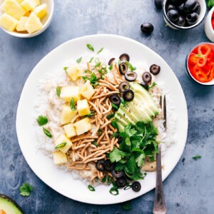 Hawaiian haystacks, a plate loaded with salad bar toppings, surrounded by additional ingredients.