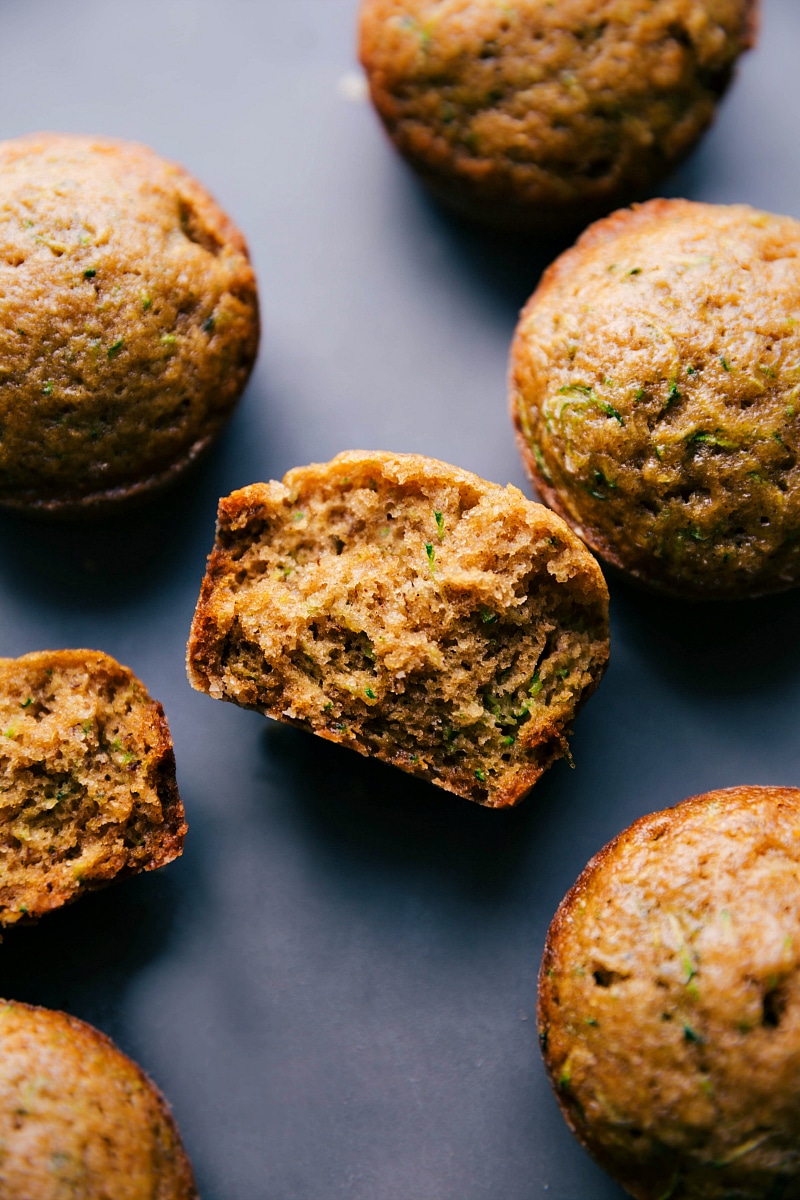 The finished healthy zucchini muffins, one split in half to reveal the moist interior.
