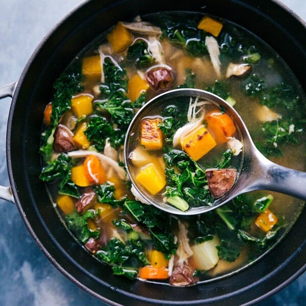 Chicken vegetable soup in the pot, with a ladle scooping up a steaming portion.