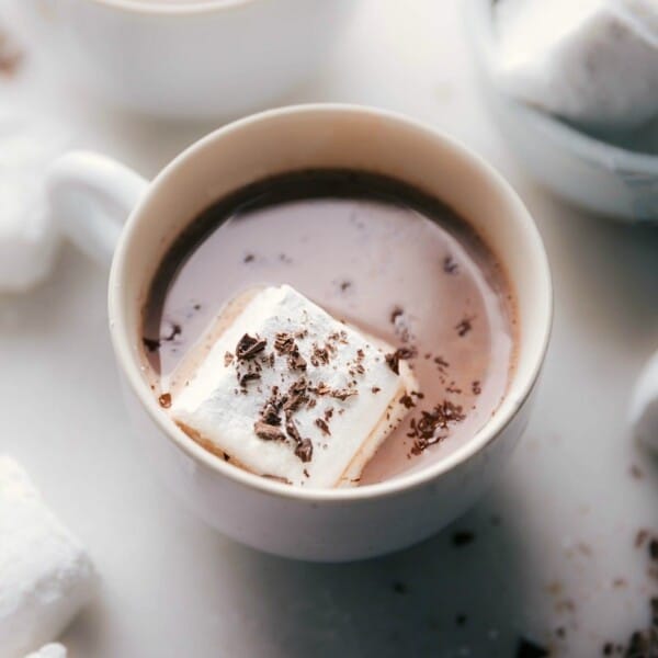 Homemade marshmallows floating in a cup of hot chocolate, topped with chocolate shavings.