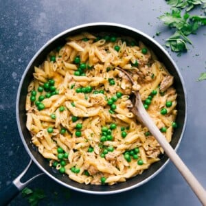 Tuna pasta in a skillet with peas and cheese, creating a savory and hearty meal.