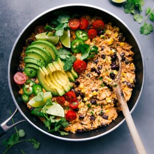 Mexican chicken and rice in the skillet, topped with fresh vegetables ready to be mixed in, and all set to be enjoyed.