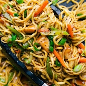 Chicken chow mein in a skillet with tongs, filled with fresh vegetables, perfectly cooked and seasoned.