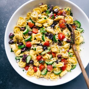 Greek tortellini salad with a spoon in the bowl, ready to be served with fresh vegetables and delicious dressing.