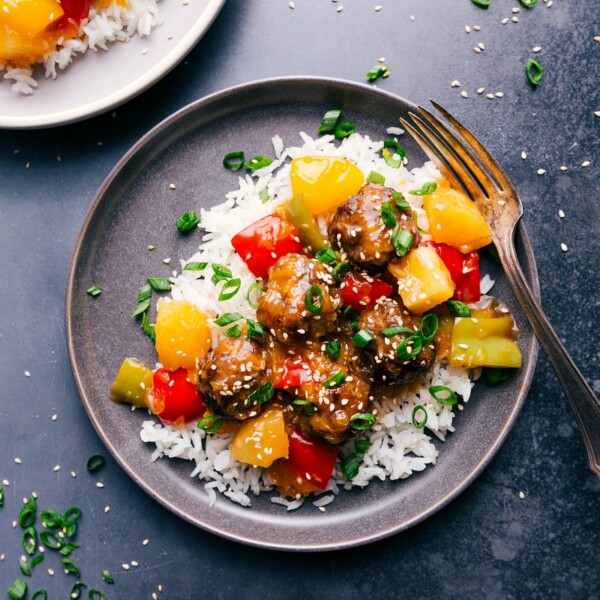 Sweet and sour meatballs over rice, garnished with fresh herbs and sesame seeds, ready to eat.