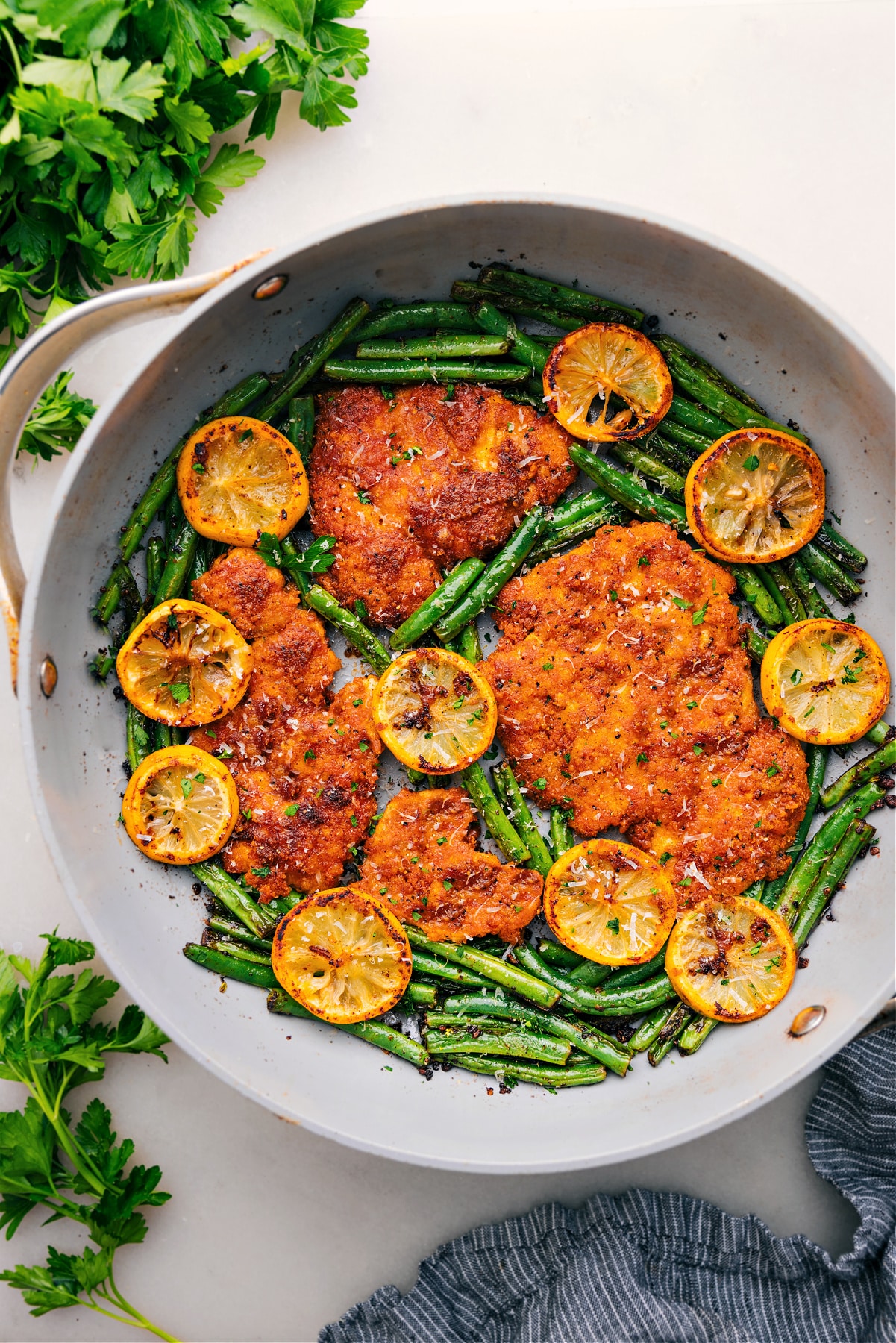 Sauté Lemon Parmesan Chicken in a skillet with green beans and fresh lemon slices.