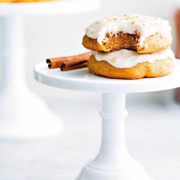 Two soft pumpkin cookies with cream cheese frosting, one with a bite taken out to reveal the fluffy interior.