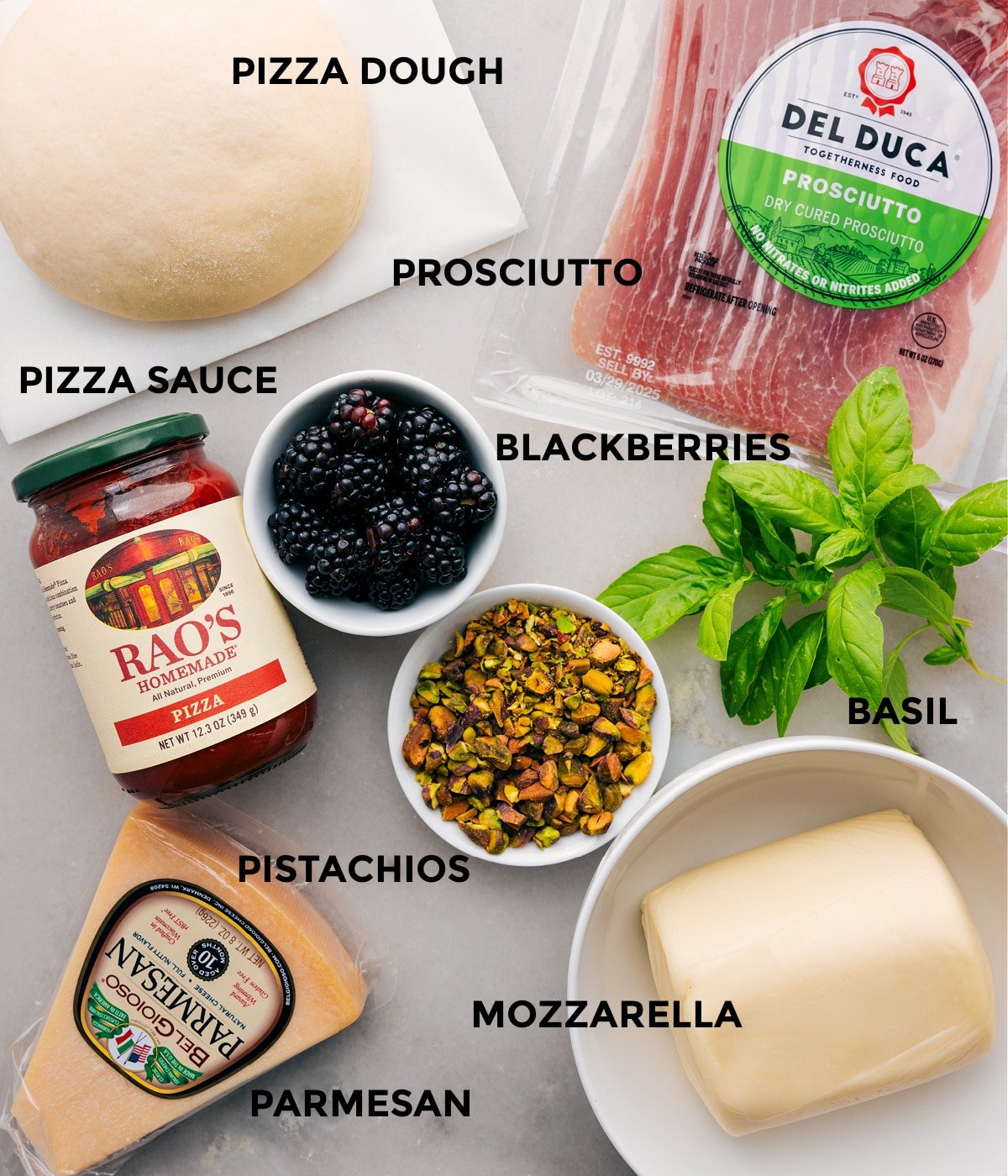 All the ingredients for this recipe are prepped and ready for easy assembly, including the dough, prosciutto, herbs, berries, sauce, cheese, and pistachios.