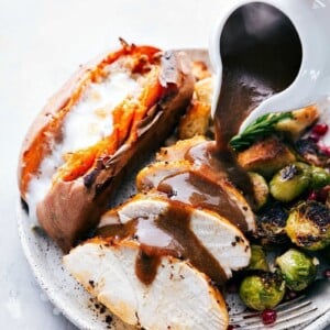 Gravy being poured over a freshly cooked Thanksgiving dinner plate, featuring a meal prepared on two sheet pans.