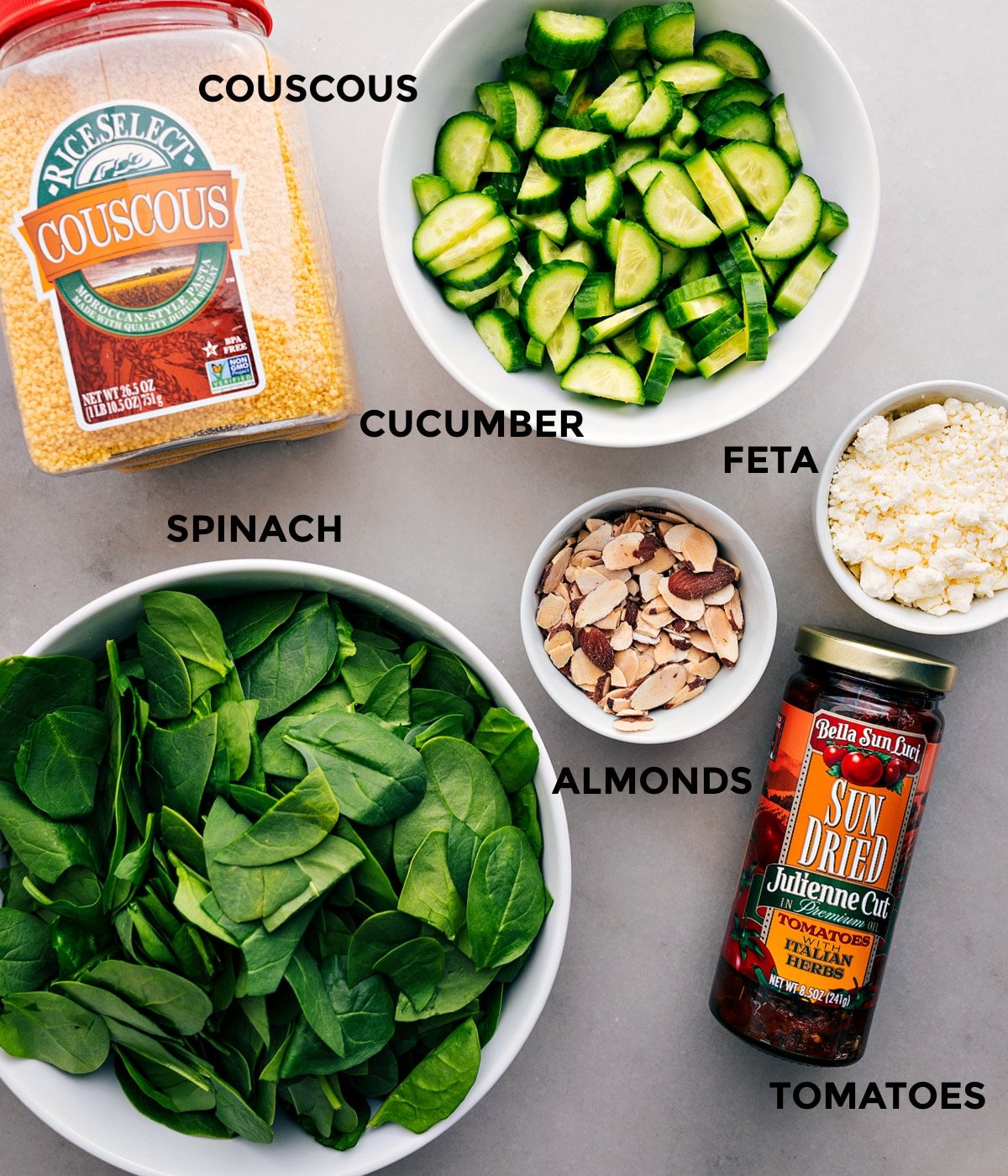 All the Couscous Mediterranean Salad ingredients prepped for easy assembly: cucumber, feta, almonds, tomatoes, spinach, and couscous.