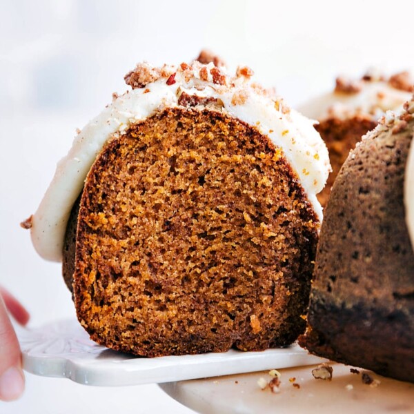 One slice of pumpkin cake with cream cheese frosting being pulled off a cake stand, revealing the moist and fluffy interior.