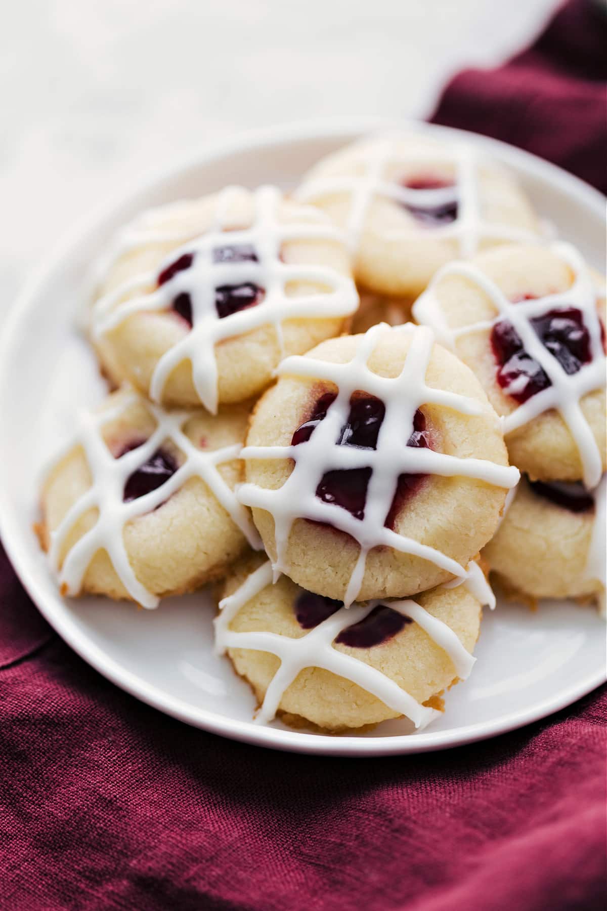 Thumbprint cookies with a yummy glaze and raspberry filling sit on a plate.