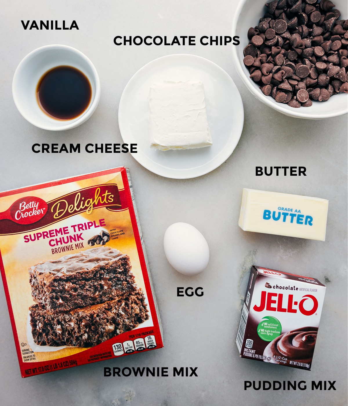 All the ingredients in this recipe including the box mix, butter, jell-o, butter, egg, chocolate chips, vanilla, and cream cheese prepped out for easy assembly.