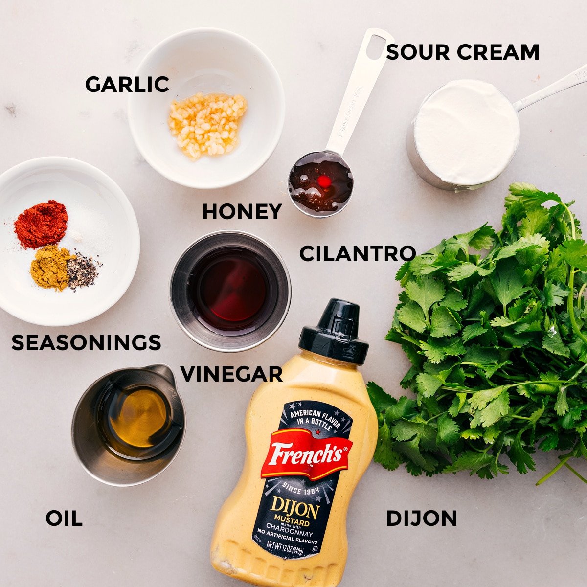 All the dressing ingredients for quinoa black bean salad prepped and ready for easy assembly, including garlic, sour cream, cilantro, honey, vinegar, mustard, and seasonings.