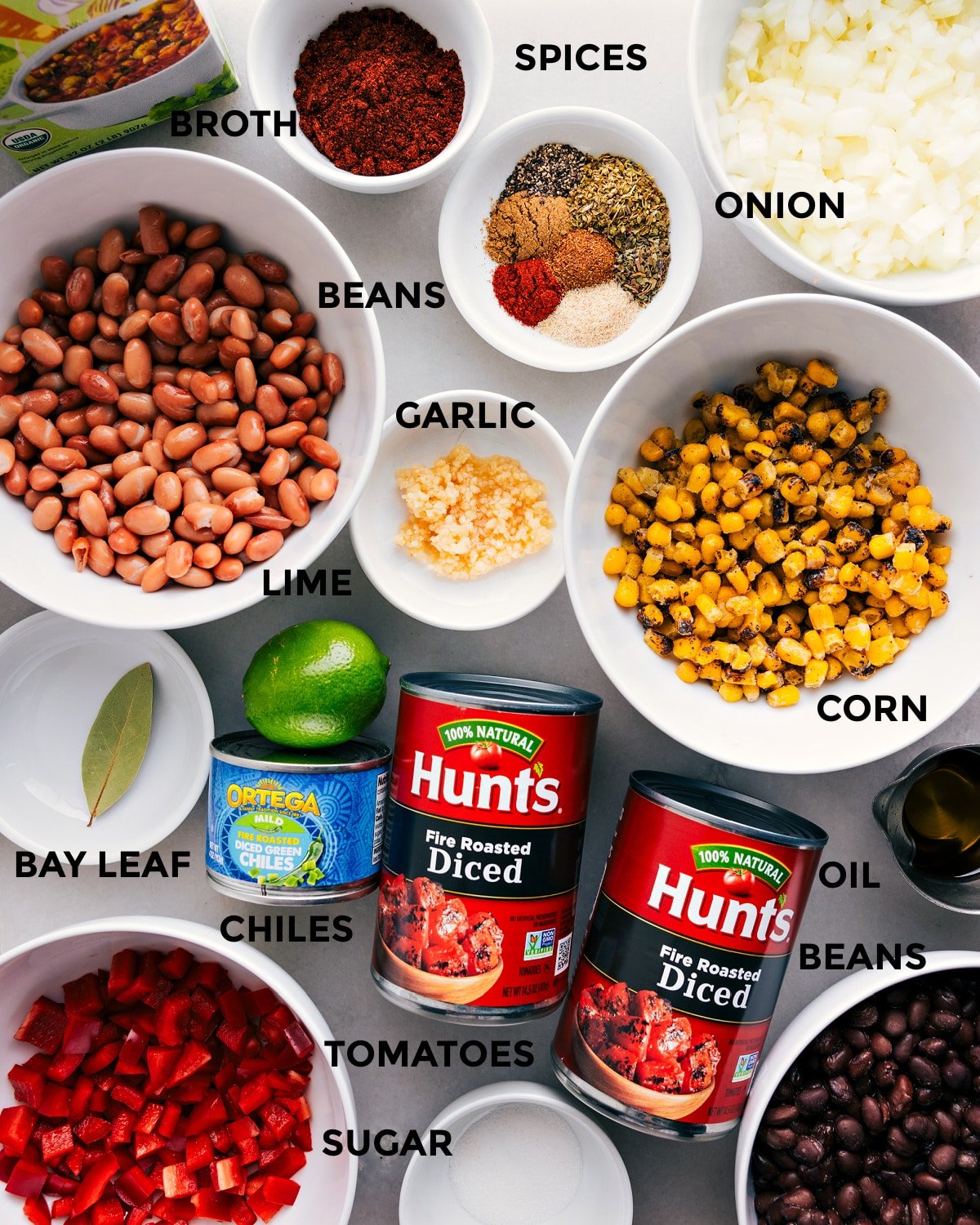 All the ingredients are prepped and ready for easy assembly—spices, veggies, beans, garlic, lime, broth, tomatoes, chiles, oil, and a bay leaf.