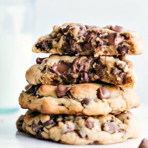 A stack of bakery-style chocolate chip cookies with the top two cookies broken in half, revealing the gooey chocolate center.