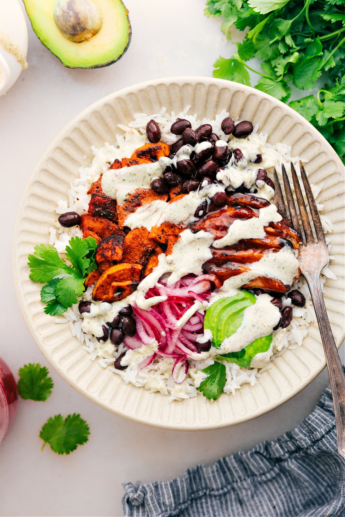 Serve the dish with rice, meat, beans, onions, avocado, and a drizzle of green goddess dressing.