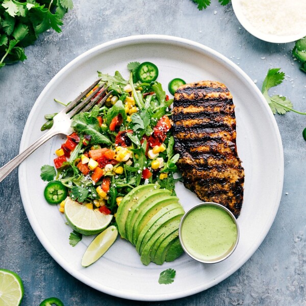 A plate filled with Peruvian chicken, a fresh salad, creamy avocado slices, and a vibrant green sauce, creating a healthy and delicious meal.