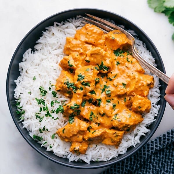 Bowl of chicken tikka masala served with rice, with a fork digging in, showcasing tender chicken pieces in a creamy, spiced sauce.