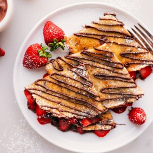 Finished Nutella crepes, generously filled with strawberries and cream, with a rich Nutella drizzle on top and a dusting of powdered sugar.