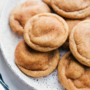 Snickerdoodle cookies arranged on a plate, fresh out of the oven, warm and inviting with a golden-brown exterior, dusted with cinnamon sugar, and packed with the best flavor.