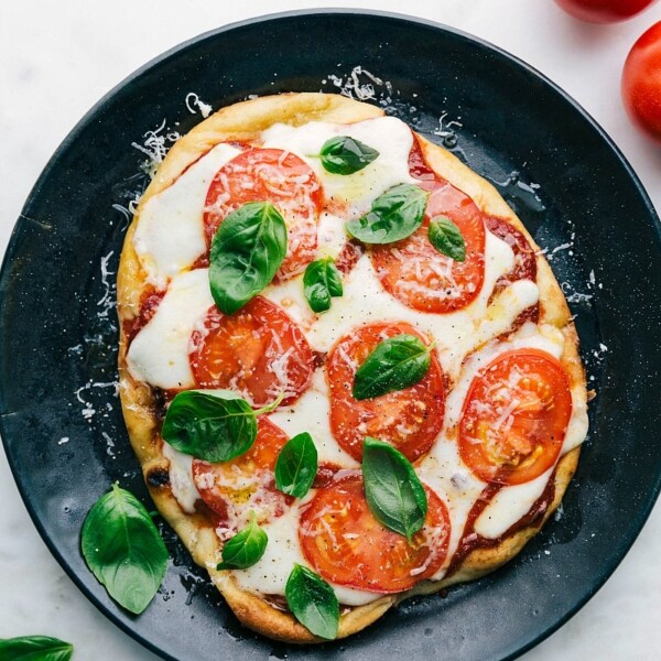 A delicious baked naan pizza on a plate, topped with fresh basil leaves, melted cheese, and vibrant toppings.