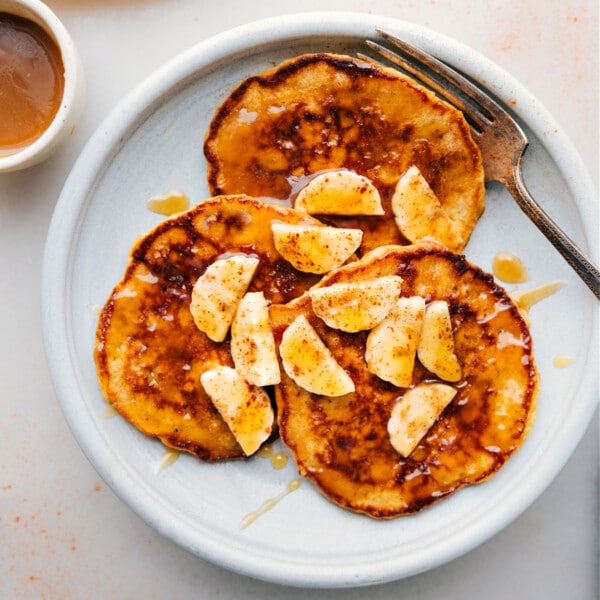 Warm banana pancakes stacked on a plate, topped with fresh banana slices and generously drizzled with syrup, creating a delicious and inviting breakfast.