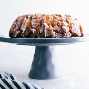 Cinnamon roll monkey bread baked and ready to eat, sitting on a cake stand, with icing dripping, delicious and full of flavor.