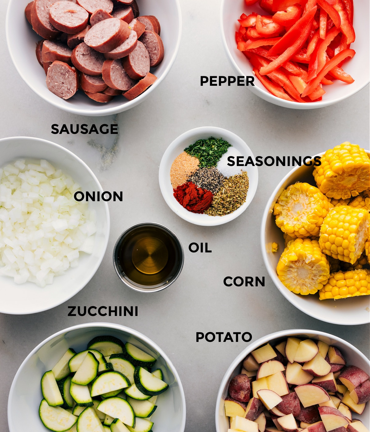All the ingredients in this recipe including sausage, pepper, onion, seasoning, corn, zucchini, potato, and oil prepped out for easy assembly.