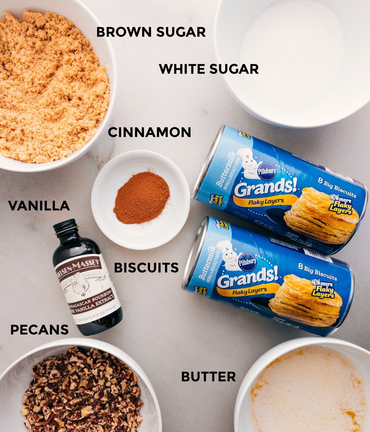 All the ingredients for this recipe are prepped and ready for easy assembly: sugars, cinnamon, biscuits, vanilla, pecans, and butter.