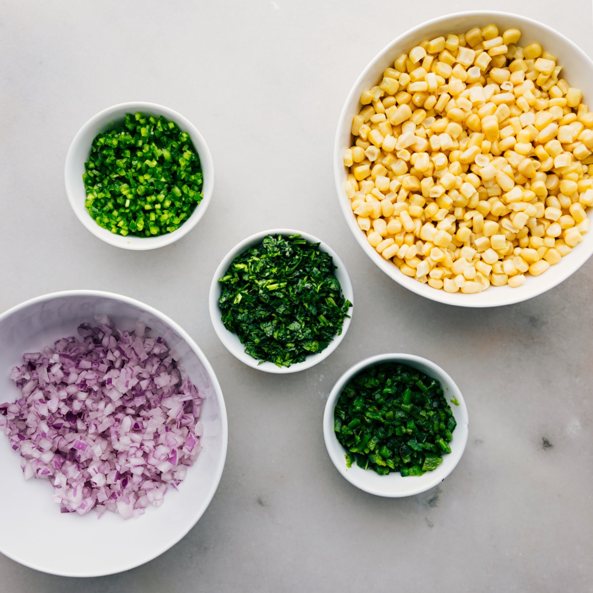 Red onion, cilantro, jalapeño, poblano, and corn prepped out on table