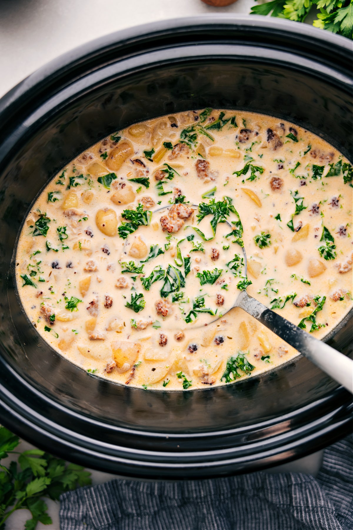 Zuppa Toscana Soup simmering in the crockpot while a ladle scoops it up.