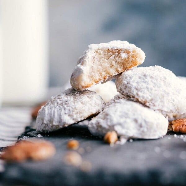 Stack of mexican wedding cookies with a bite taken out of one, showing the fluffy interior.