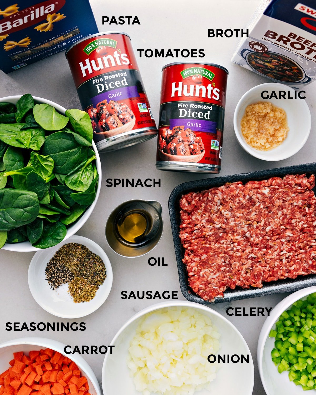 All the ingredients—beef broth, garlic, tomatoes, pasta, sausage, spinach, oil, seasonings, and veggies—are prepped for easy assembly.