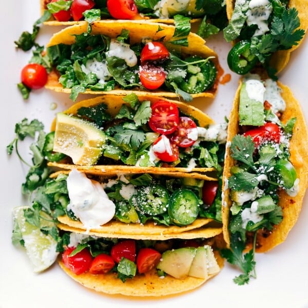 Baked chicken tacos fresh out of the oven, topped with fresh vegetables, herbs, and a delicious sauce.