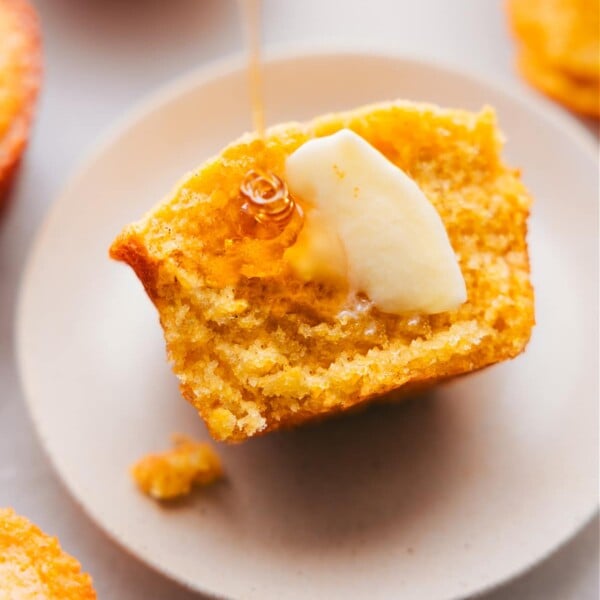 Freshly baked cornbread muffin, cut in half to reveal its fluffy interior, served with butter and honey on top.