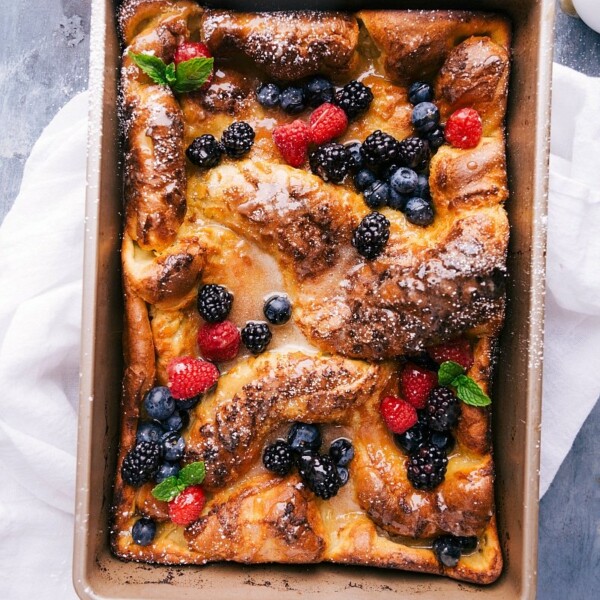 Dutch baby pancake freshly baked, topped with an array of fresh fruit and drizzled with syrup.