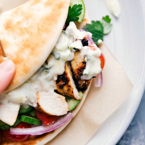 A chicken gyro wrapped in a soft pita, filled with seasoned chicken, fresh vegetables, and tzatziki sauce spilling out the sides, prepared to be eaten.