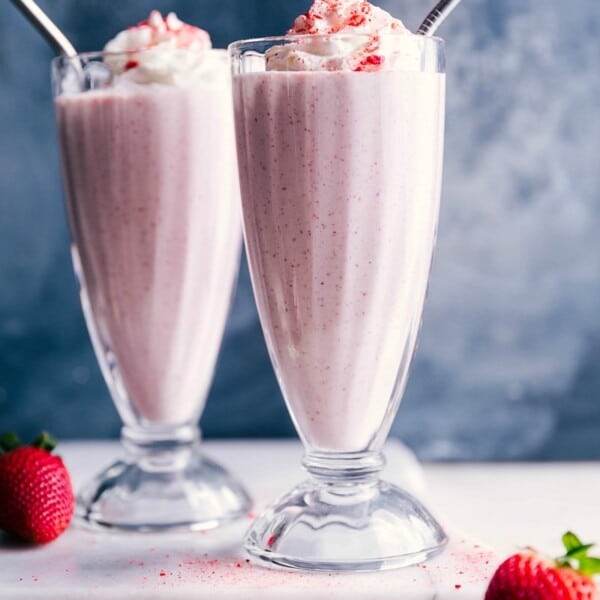 Two strawberry milkshakes with whipped cream on top and straws in them, a thick and delicious dessert.