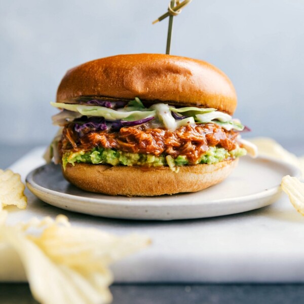 BBQ chicken sandwich with an abundance of BBQ chicken spilling out, served on a plate and ready to be eaten.