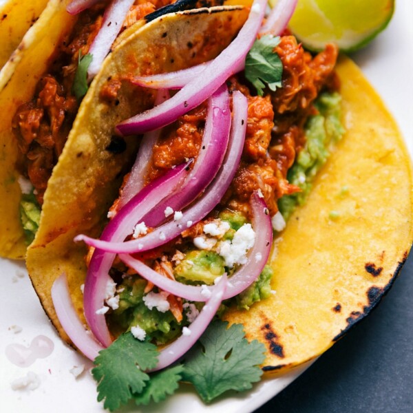 Chicken tinga tacos fully assembled and ready to be enjoyed, topped with red onions, cilantro, cheese, and more.