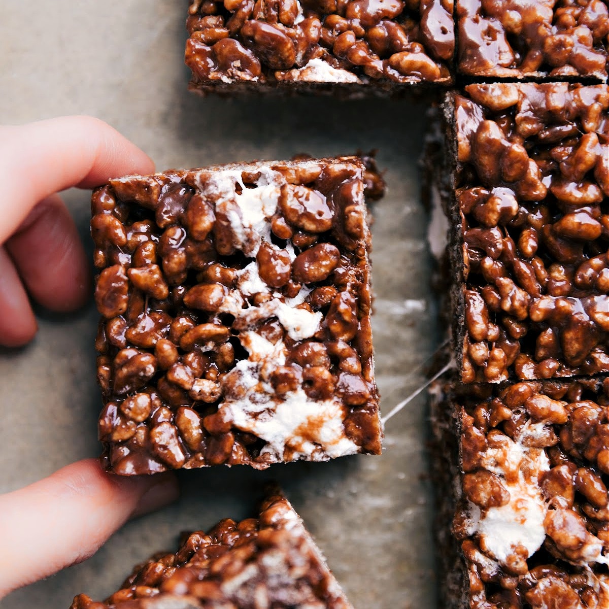 A chocolate rice krispie treat cut out and being pulled away showing the gooey marshmallow texture.