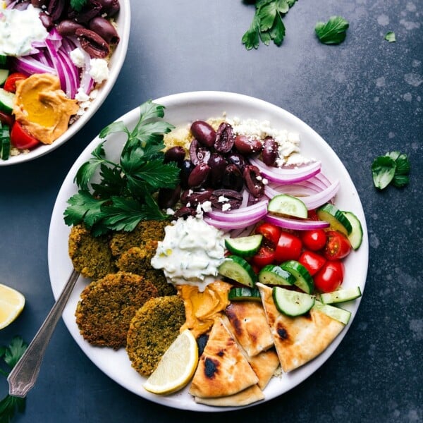 Baked falafel served on a plate with pita bread, tzatziki sauce, olives, onions, tomatoes, and cucumbers.