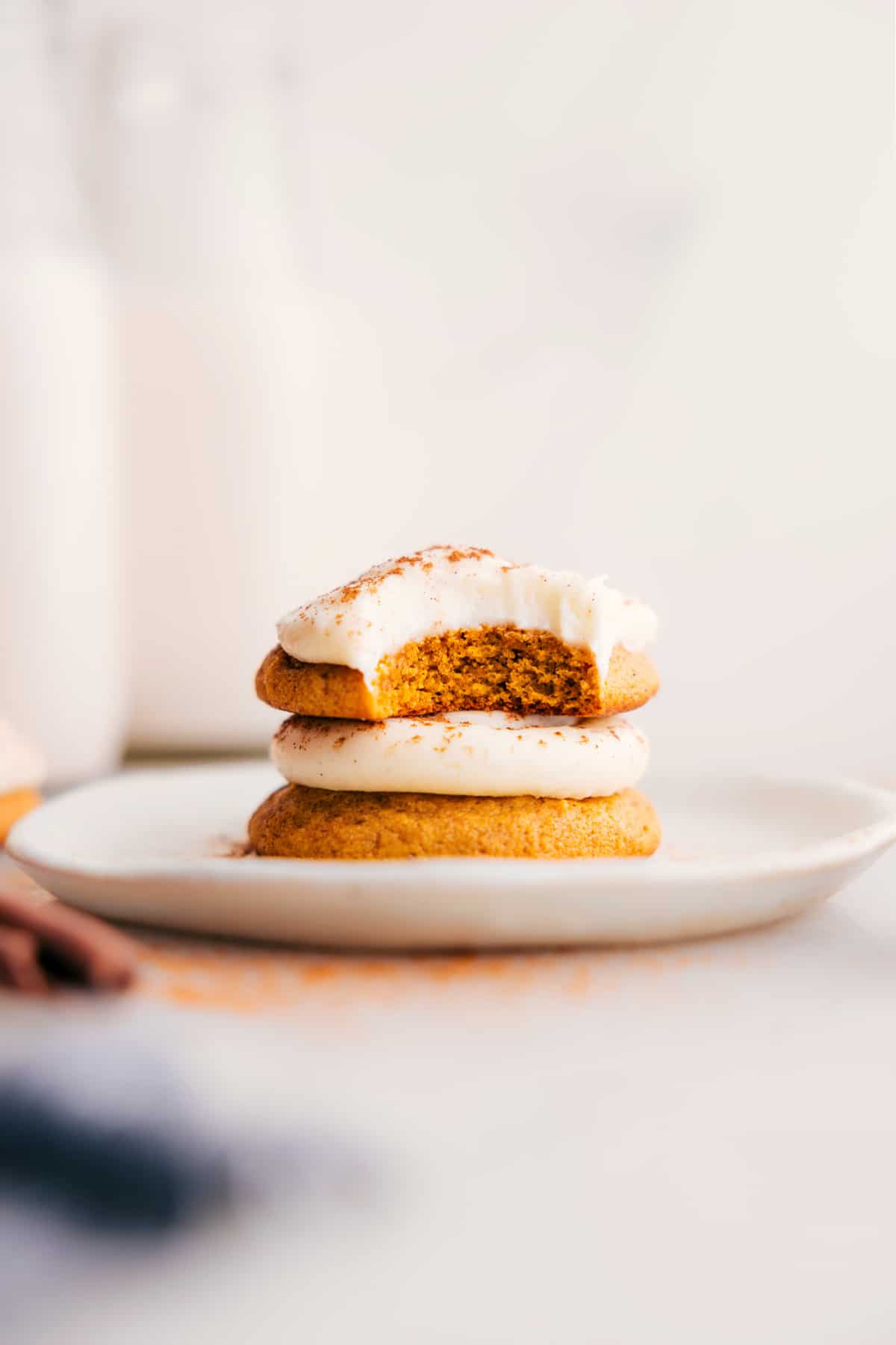 Pumpkin Cookies with Cream Cheese Frosting stack on a plate, the top one with a bite missing.