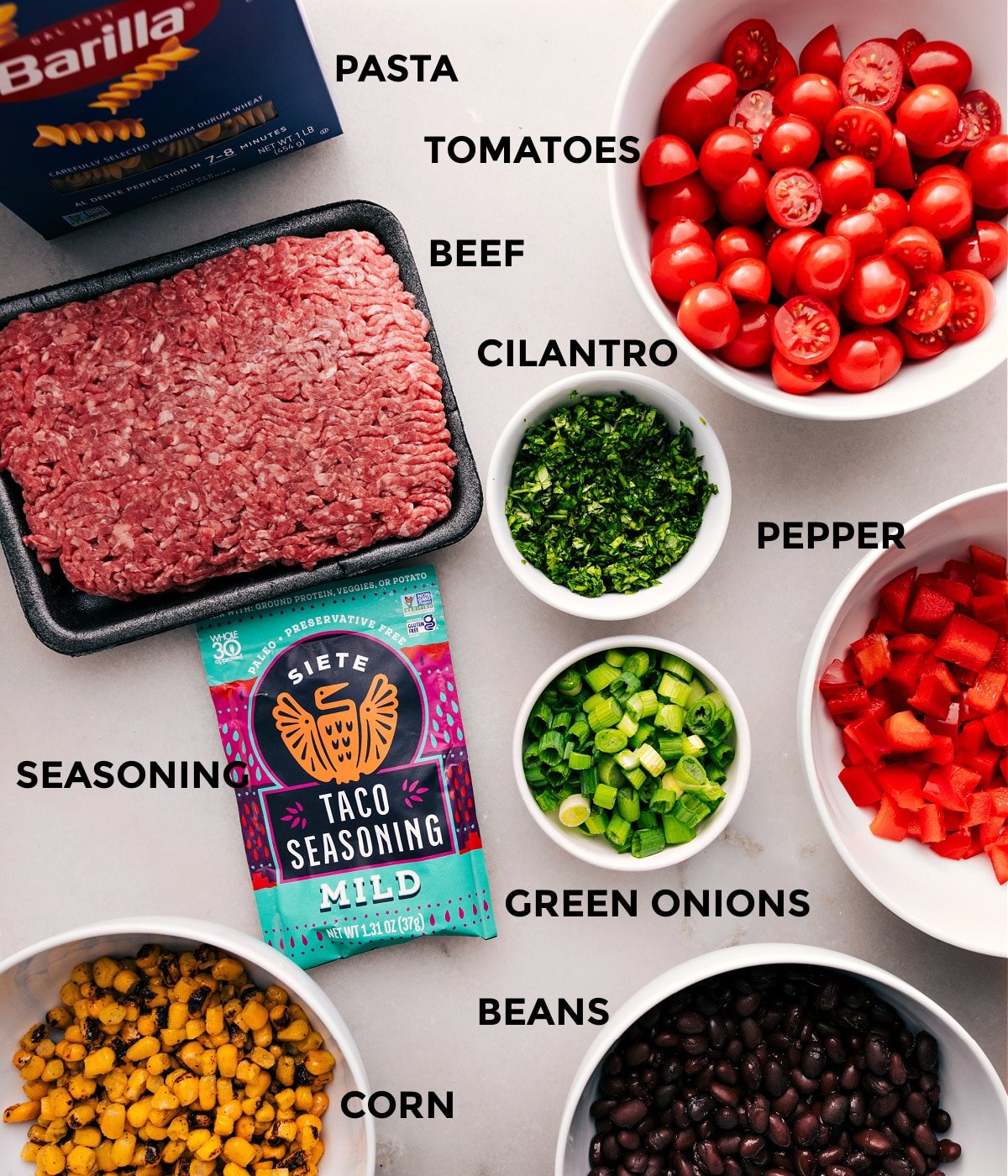 All the ingredients—pasta, meat, tomatoes, cilantro, pepper, green onions, seasoning, beans, and corn—are prepped and ready for easy assembly.