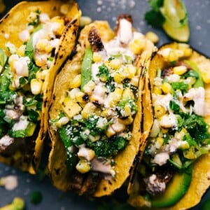 Finished steak taco recipe, with tacos side by side, stuffed with delicious meat, corn salsa, and various toppings.