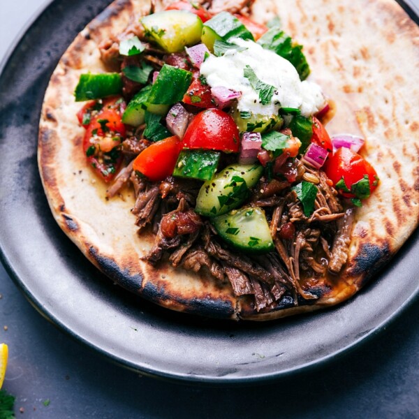 Juicy beef gyro on soft pita bread, topped with crisp fresh vegetables and a generous drizzle of tangy sauce, creating a flavorful and satisfying meal.