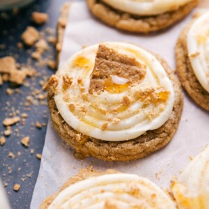 Frosted honey graham cookies topped with creamy frosting, garnished with graham cracker crumbs, a drizzle of honey, and a large graham cracker piece.