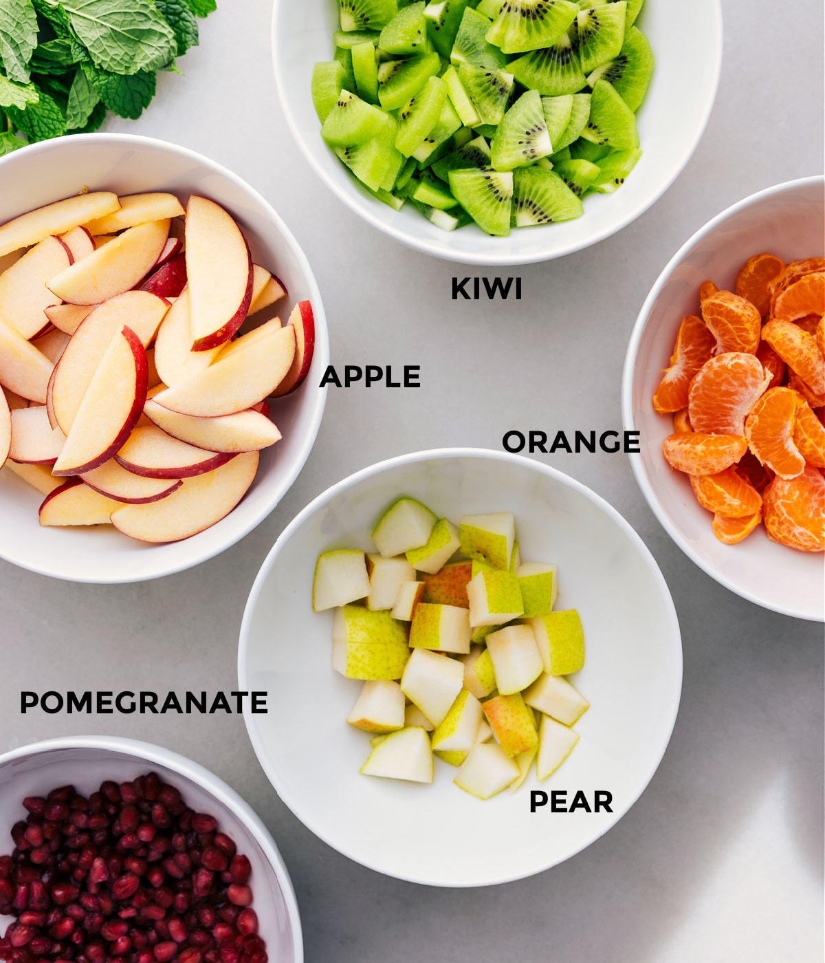 All the ingredients for this dish are prepped for easy assembly: kiwis, apples, oranges, pears, and pomegranates.