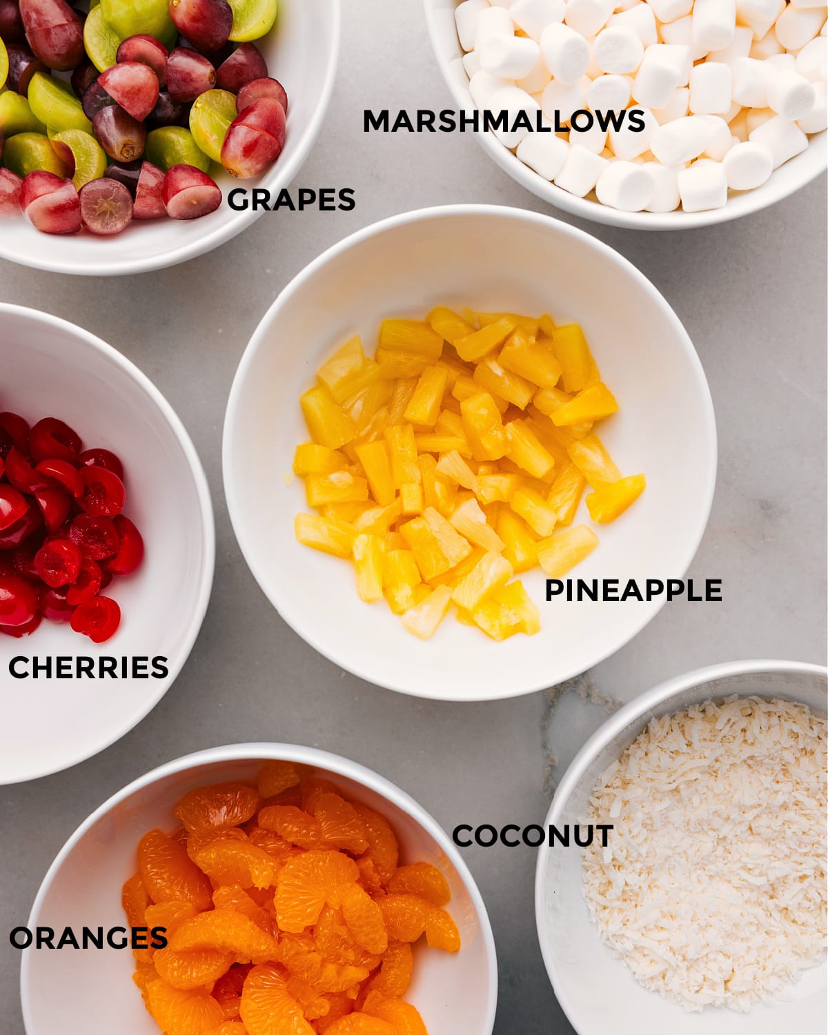 The ingredients in this recipe include pineapple, marshmallows, grapes, cherries, coconut, and oranges.